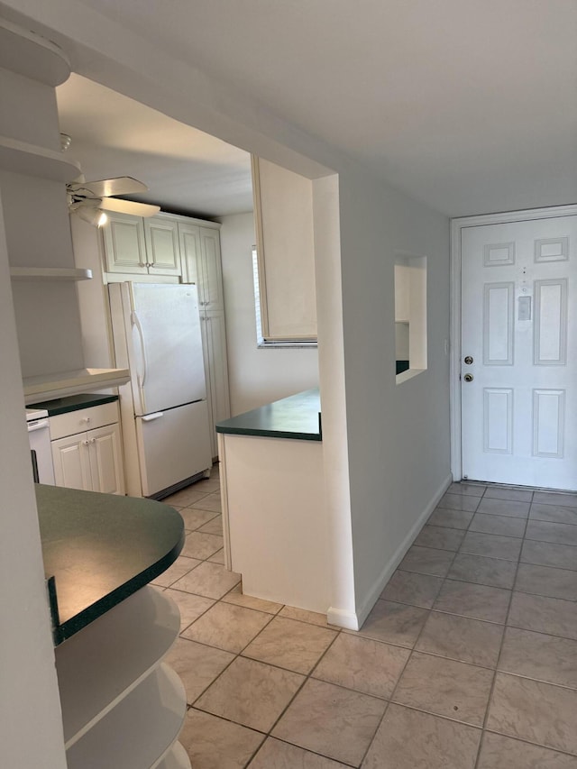 kitchen featuring freestanding refrigerator, ceiling fan, dark countertops, and light tile patterned floors