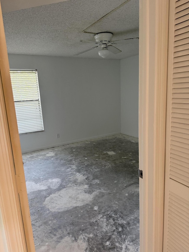 empty room with a textured ceiling, ceiling fan, and unfinished concrete flooring