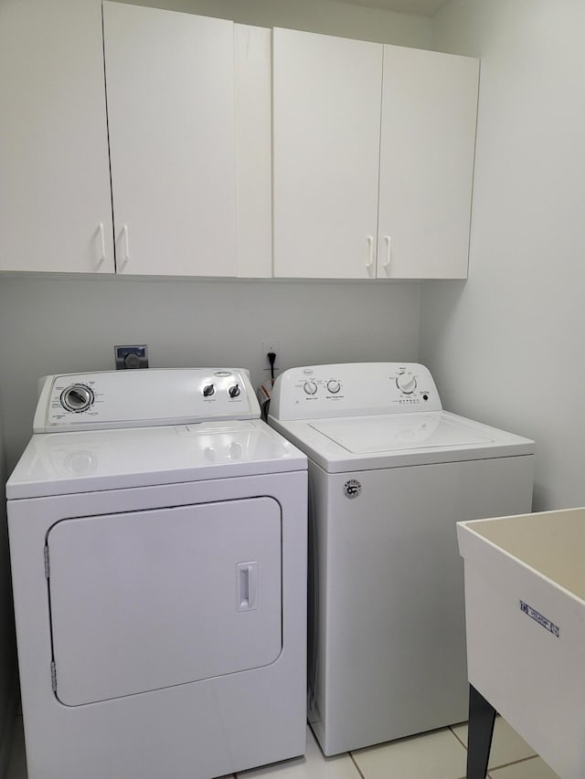 clothes washing area featuring sink, light tile patterned floors, washing machine and dryer, and cabinets