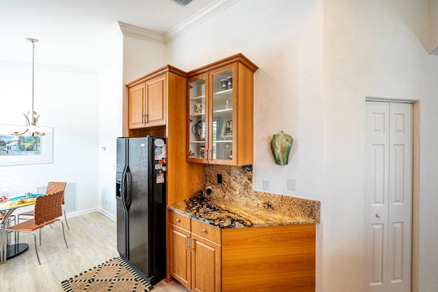 kitchen featuring pendant lighting, dark stone counters, crown molding, black fridge, and light hardwood / wood-style flooring