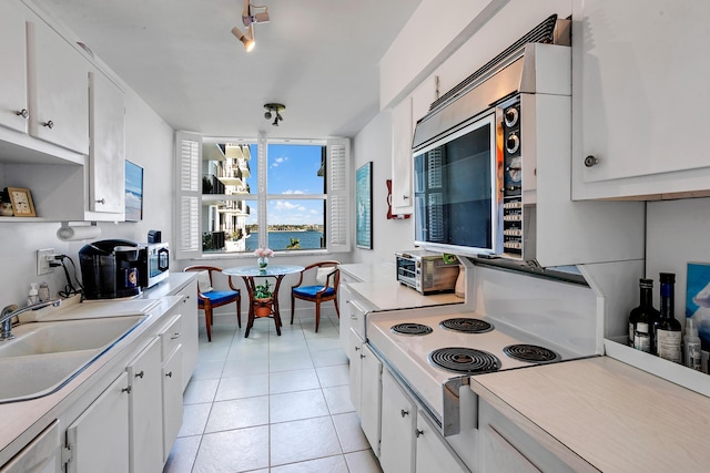 kitchen with light tile patterned floors, cooktop, sink, and white cabinets