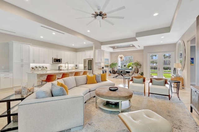 living room with french doors, ceiling fan, a tray ceiling, and sink