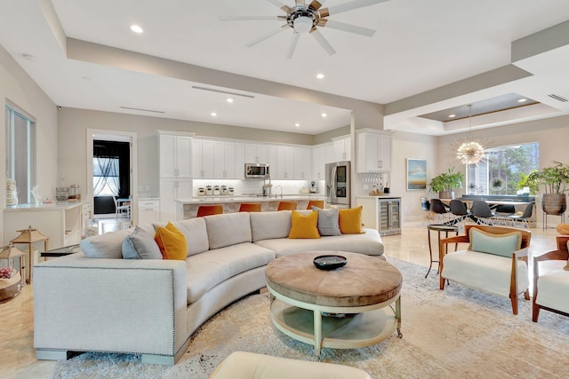 living room with beverage cooler, a tray ceiling, and ceiling fan with notable chandelier