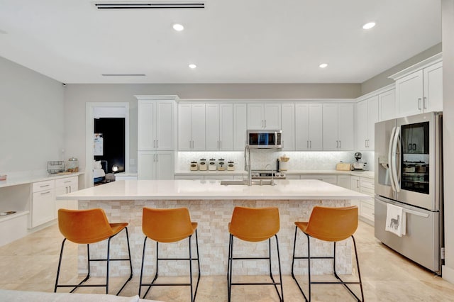 kitchen with sink, white cabinetry, backsplash, stainless steel appliances, and a center island with sink