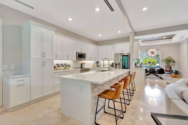 kitchen with sink, appliances with stainless steel finishes, white cabinetry, light stone counters, and decorative backsplash