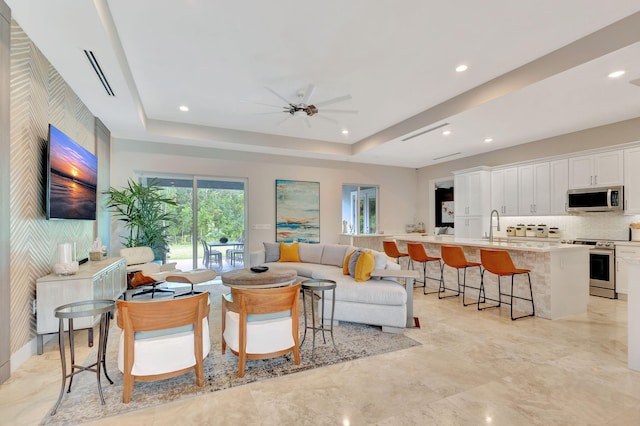 living room with sink, a tray ceiling, and ceiling fan