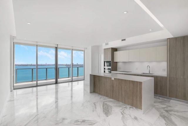 kitchen featuring white cabinetry, a water view, a center island, a wall of windows, and black appliances