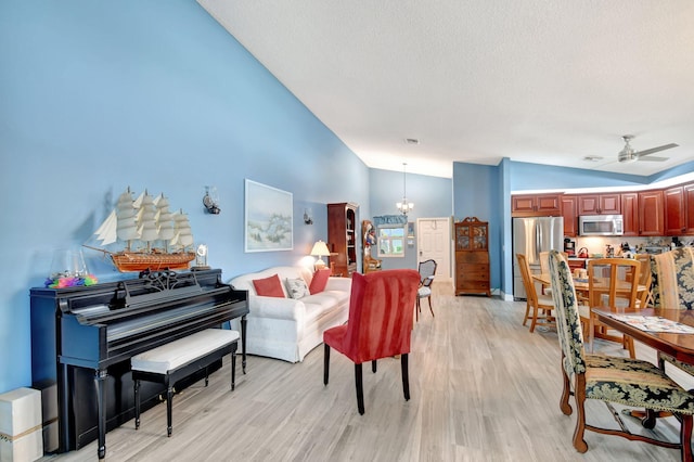 living room featuring lofted ceiling, ceiling fan with notable chandelier, a textured ceiling, and light wood-type flooring