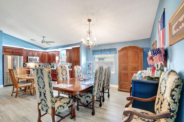 dining area with vaulted ceiling, ceiling fan with notable chandelier, a textured ceiling, and light hardwood / wood-style flooring