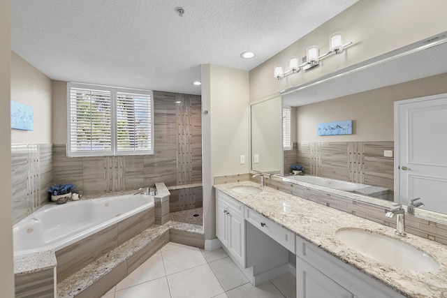 bathroom with tile patterned floors, tiled tub, vanity, and a textured ceiling