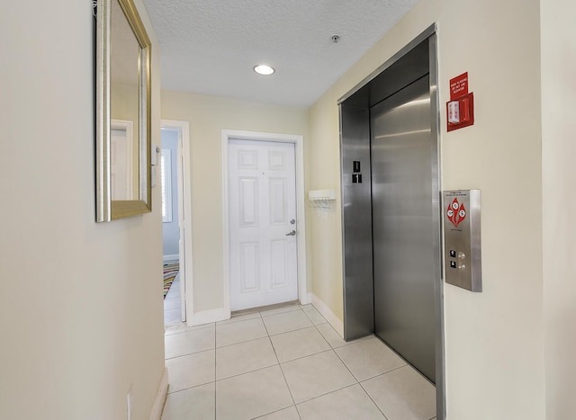 corridor with elevator, a textured ceiling, and light tile patterned floors