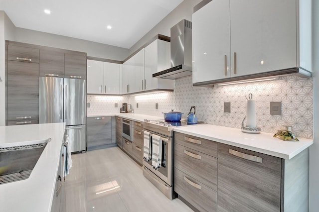 kitchen with gray cabinets, tasteful backsplash, white cabinetry, stainless steel appliances, and wall chimney exhaust hood