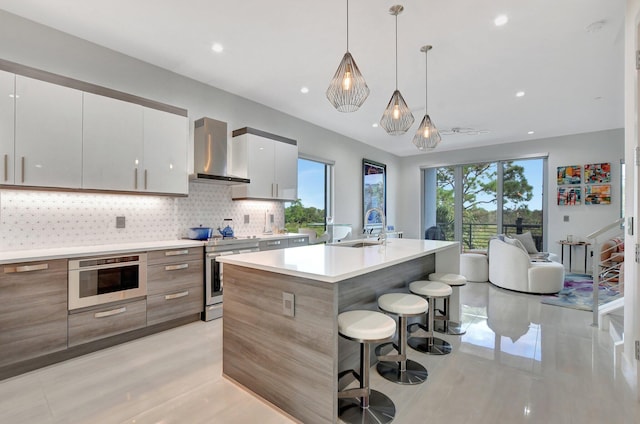 kitchen with wall chimney range hood, sink, appliances with stainless steel finishes, white cabinetry, and decorative light fixtures