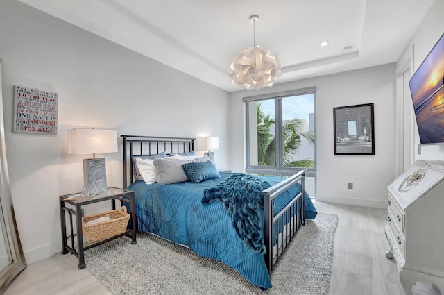 bedroom featuring a tray ceiling, light hardwood / wood-style floors, and a notable chandelier