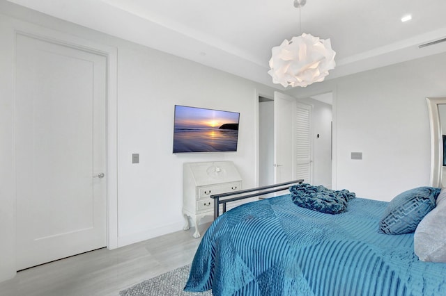 bedroom with a raised ceiling, a notable chandelier, and light hardwood / wood-style floors