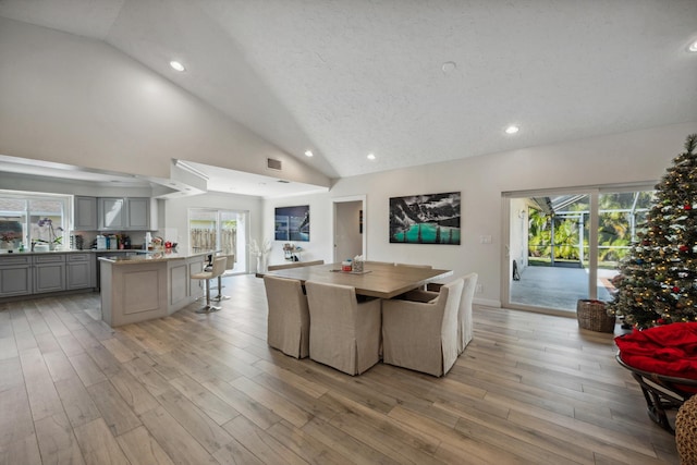 dining room featuring lofted ceiling, a textured ceiling, and light hardwood / wood-style flooring