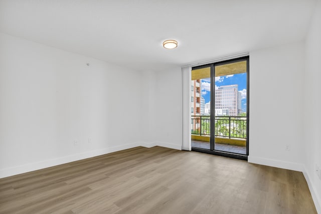 empty room featuring baseboards, light wood-style floors, expansive windows, and a city view