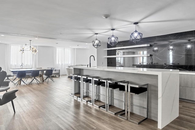 kitchen with wood finished floors, a kitchen breakfast bar, light countertops, modern cabinets, and pendant lighting