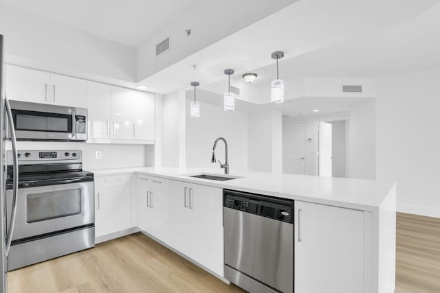 kitchen with light countertops, appliances with stainless steel finishes, white cabinets, a sink, and a peninsula