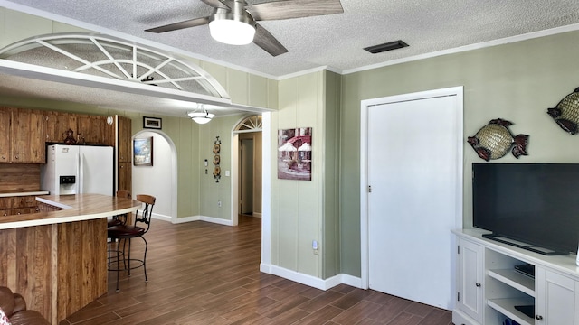 kitchen featuring dark wood-type flooring, ornamental molding, a kitchen breakfast bar, white fridge with ice dispenser, and ceiling fan