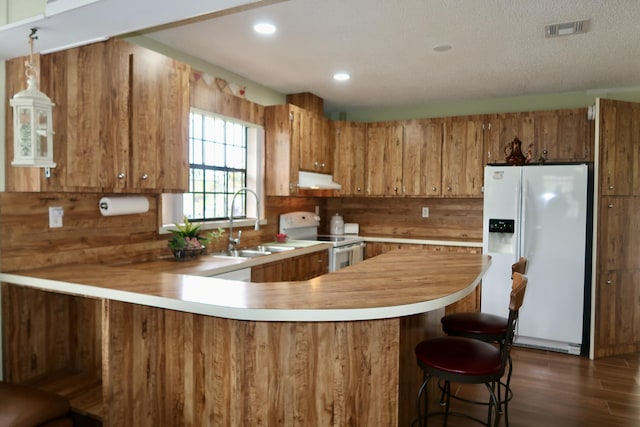 kitchen featuring sink, a textured ceiling, dark hardwood / wood-style floors, kitchen peninsula, and white appliances