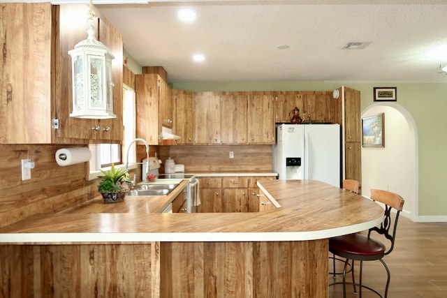 kitchen featuring sink, hardwood / wood-style flooring, white fridge with ice dispenser, kitchen peninsula, and a textured ceiling