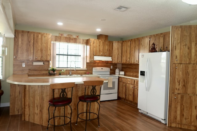 kitchen with sink, white appliances, a breakfast bar, dark hardwood / wood-style floors, and kitchen peninsula