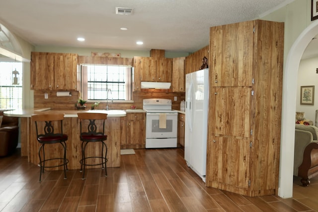 kitchen with dark hardwood / wood-style flooring, sink, white appliances, and a kitchen bar