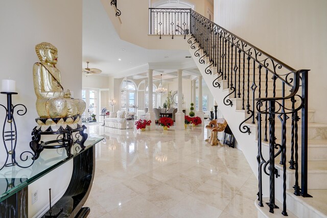 entryway featuring ceiling fan with notable chandelier, a high ceiling, and ornate columns