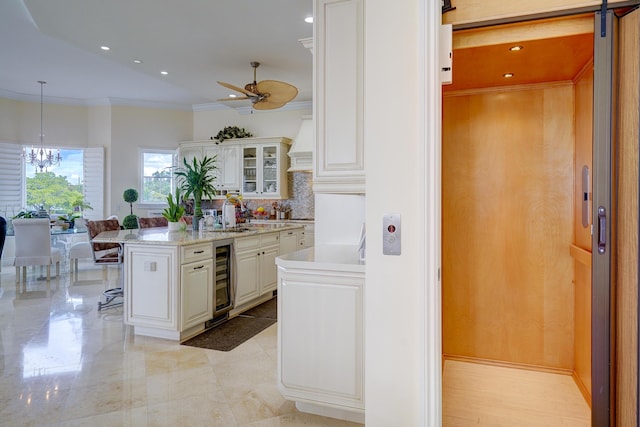 kitchen with white cabinetry, hanging light fixtures, wine cooler, an island with sink, and elevator