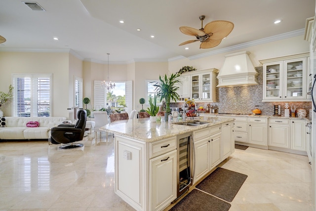 kitchen with sink, hanging light fixtures, a center island with sink, custom exhaust hood, and beverage cooler