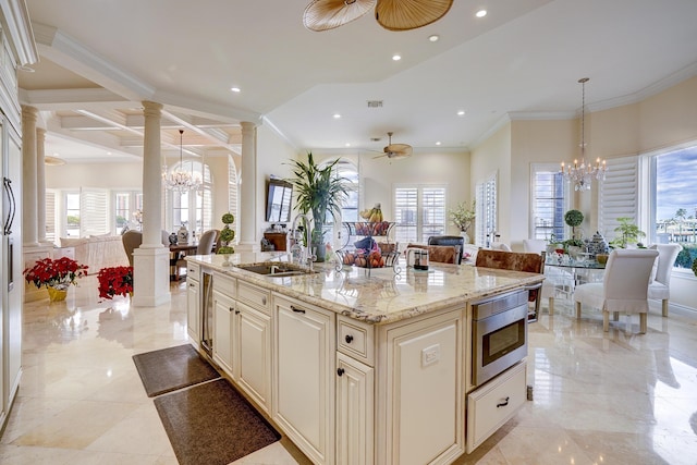 kitchen with decorative light fixtures, decorative columns, sink, a center island with sink, and cream cabinetry