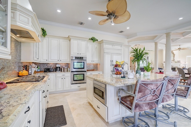 kitchen with custom exhaust hood, built in appliances, a kitchen breakfast bar, decorative columns, and backsplash