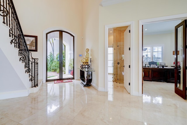 foyer with french doors, a towering ceiling, and ornamental molding