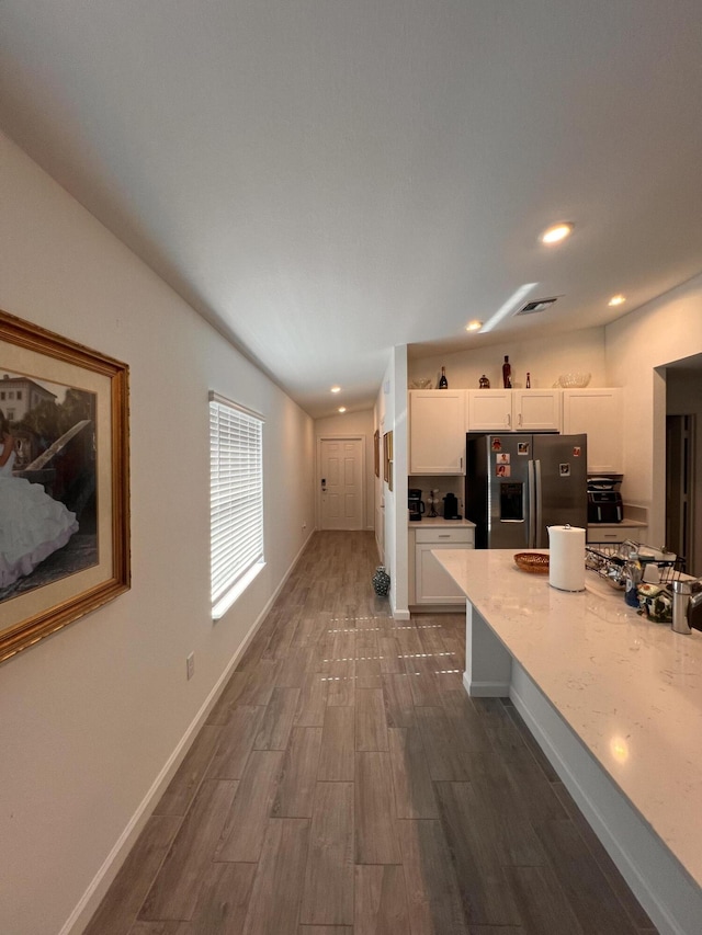 kitchen with white cabinetry, dark hardwood / wood-style floors, stainless steel fridge, and light stone counters