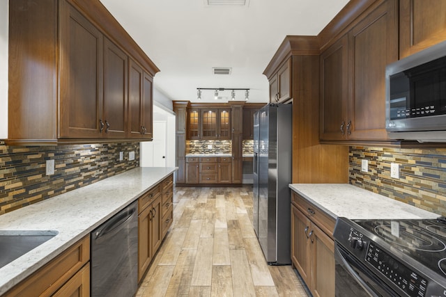 kitchen with rail lighting, backsplash, light stone counters, black appliances, and light wood-type flooring