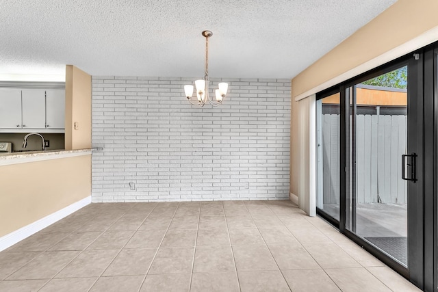 unfurnished dining area with light tile patterned floors, sink, an inviting chandelier, a textured ceiling, and brick wall