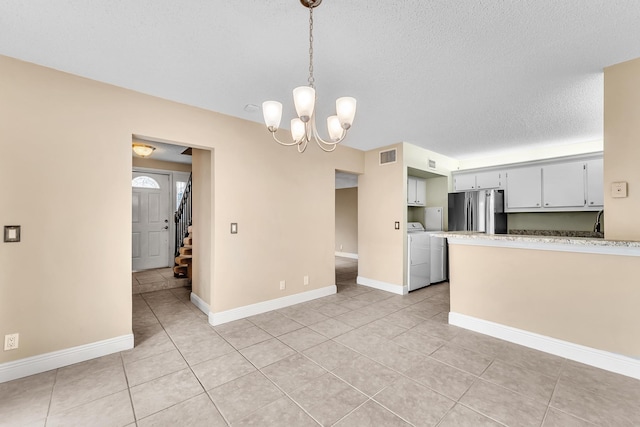 kitchen with stainless steel refrigerator, hanging light fixtures, washer and dryer, a textured ceiling, and a chandelier