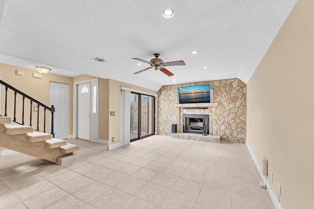 unfurnished living room featuring ceiling fan, a stone fireplace, light tile patterned floors, and a textured ceiling