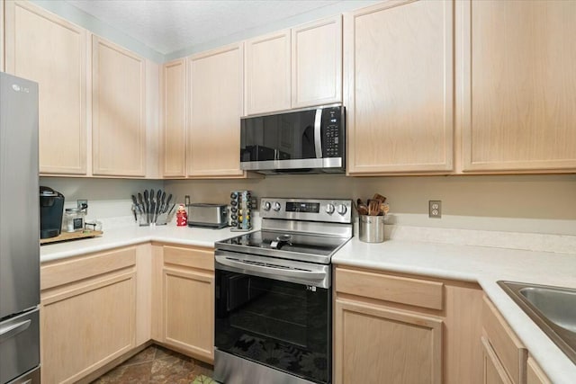 kitchen with light brown cabinetry, sink, a textured ceiling, appliances with stainless steel finishes, and dark tile patterned floors