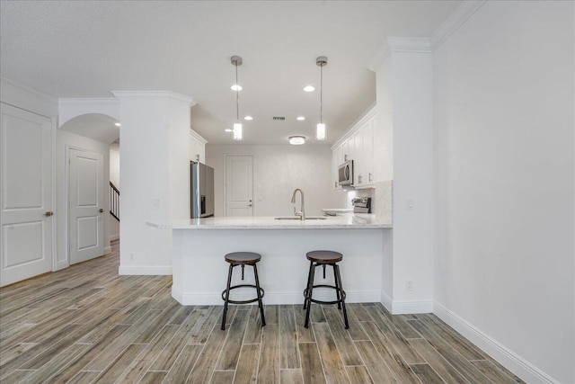 kitchen with a breakfast bar area, decorative light fixtures, kitchen peninsula, stainless steel appliances, and white cabinets