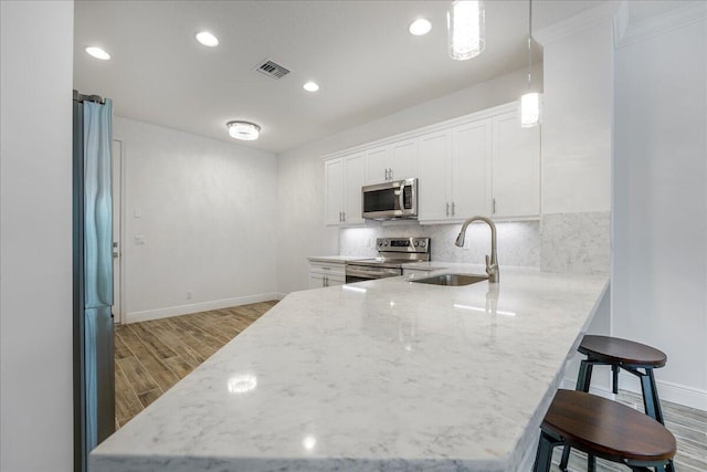 kitchen featuring sink, appliances with stainless steel finishes, white cabinetry, a kitchen breakfast bar, and kitchen peninsula