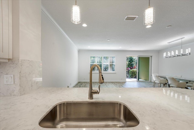 kitchen with decorative light fixtures, sink, ornamental molding, light stone counters, and light wood-type flooring