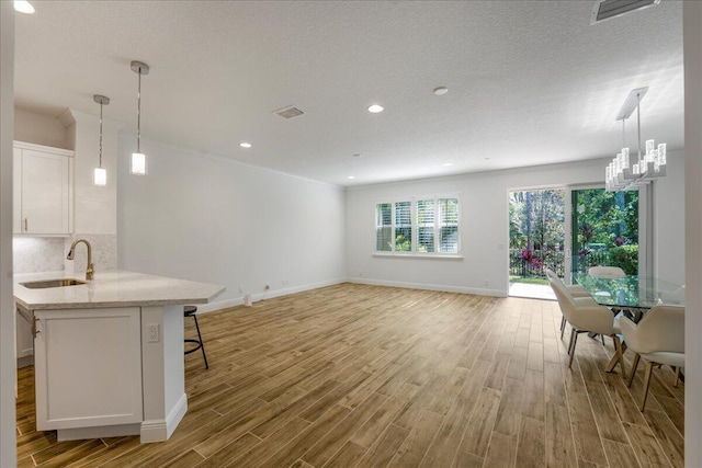 kitchen featuring sink, light hardwood / wood-style flooring, hanging light fixtures, and white cabinets