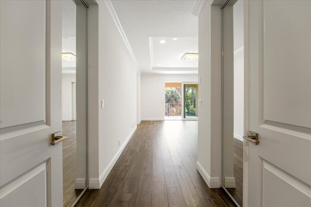 hall featuring dark hardwood / wood-style flooring, a tray ceiling, ornamental molding, and a textured ceiling