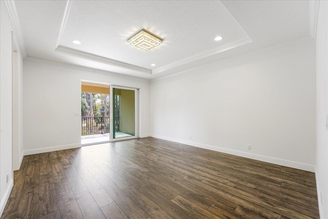 empty room featuring dark wood-type flooring, ornamental molding, a tray ceiling, and a textured ceiling