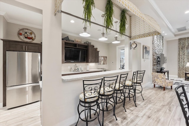 kitchen featuring dark brown cabinetry, sink, stainless steel fridge, and a kitchen bar