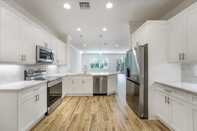 kitchen with appliances with stainless steel finishes, decorative light fixtures, sink, white cabinets, and kitchen peninsula