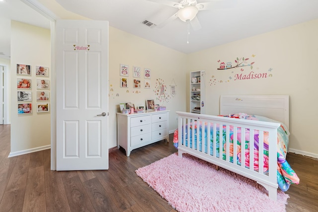 bedroom featuring a crib, dark wood-type flooring, and ceiling fan