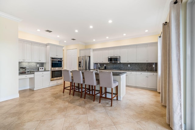 kitchen featuring a kitchen breakfast bar, stainless steel appliances, an island with sink, and white cabinets